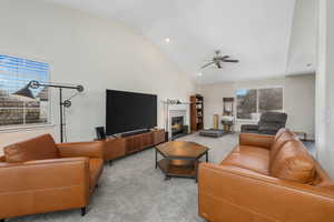 Living area with high vaulted ceiling, a fireplace with flush hearth, carpet, and ceiling fan