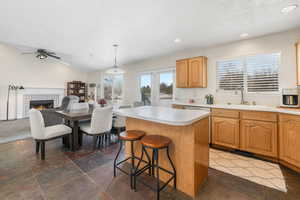 Kitchen with a sink, a kitchen island, a fireplace, light countertops, and lofted ceiling