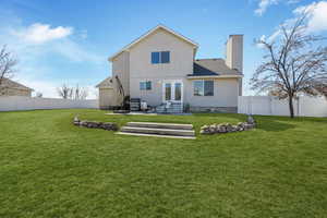 Rear view of property featuring entry steps, a yard, a fenced backyard, and a chimney