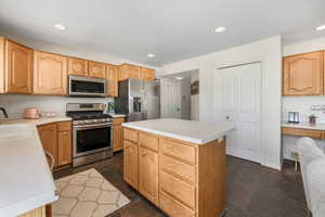 Kitchen featuring stone tile floors, a sink, stainless steel appliances, light countertops, and a center island