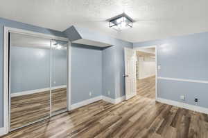 Unfurnished bedroom with a closet, a textured ceiling, baseboards, and wood finished floors