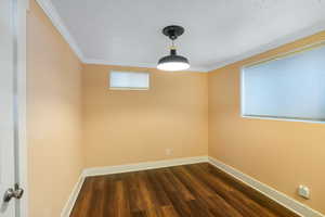 Empty room featuring crown molding, a textured ceiling, baseboards, and dark wood-style flooring