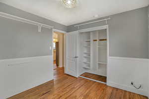 Unfurnished bedroom with a closet, wainscoting, and wood finished floors