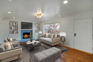 Living room featuring ornamental molding, recessed lighting, a premium fireplace, and wood finished floors