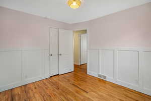 Unfurnished bedroom featuring wainscoting, wood finished floors, and visible vents