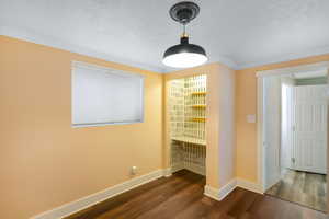 Unfurnished dining area featuring dark wood-style flooring, crown molding, a textured ceiling, and baseboards