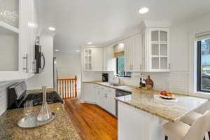 Kitchen featuring light wood finished floors, a peninsula, stainless steel appliances, white cabinetry, and a sink