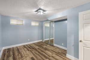 Finished below grade area featuring a textured ceiling, baseboards, and wood finished floors