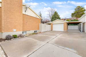 View of side of property with an outbuilding, a garage, brick siding, fence, and driveway