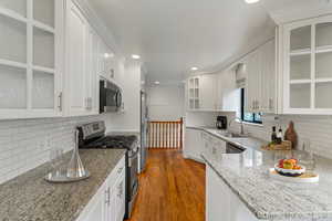 Kitchen with stainless steel appliances, wood finished floors, a sink, white cabinetry, and decorative backsplash