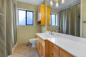 Bathroom featuring baseboards, toilet, curtained shower, tile patterned flooring, and vanity