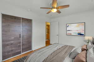 Bedroom featuring a ceiling fan, a closet, crown molding, and wood finished floors