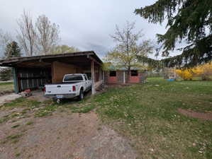 View of property exterior featuring a lawn, driveway, an outbuilding, and an attached carport
