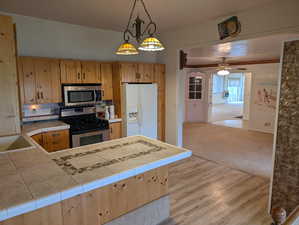 Kitchen featuring a ceiling fan, tasteful backsplash, tile counters, stainless steel appliances, and a peninsula
