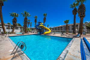 Community pool with playground community, fence, a water slide, and a patio