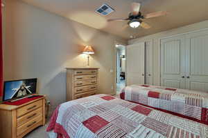 Carpeted bedroom with ceiling fan, two closets, visible vents, and baseboards