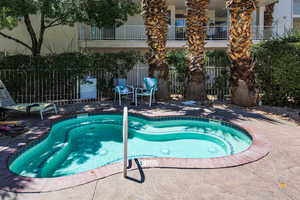 View of swimming pool with fence, a community hot tub, and a patio