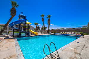 Community pool with playground community, a patio area, fence, and a water slide