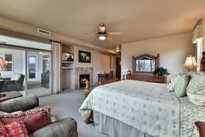 Carpeted bedroom with access to outside, visible vents, ceiling fan, and a tiled fireplace