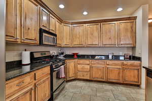 Kitchen with stainless steel appliances, recessed lighting, brown cabinets, and dark stone countertops