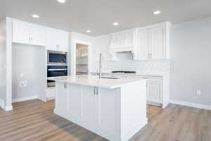 Kitchen featuring appliances with stainless steel finishes, white cabinets, light wood-style floors, and backsplash