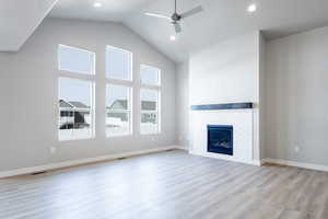 Unfurnished living room featuring a ceiling fan, a brick fireplace, wood finished floors, high vaulted ceiling, and baseboards