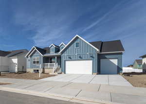 View of front of property featuring driveway, a shingled roof, an attached garage, covered porch, and board and batten siding