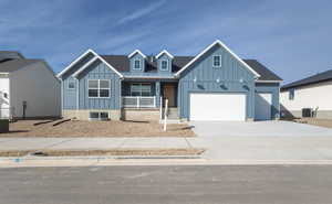 View of front facade featuring covered porch, cooling unit, board and batten siding, and concrete driveway