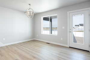 Unfurnished room featuring light wood-type flooring, an inviting chandelier, baseboards, and visible vents