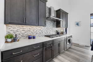 Kitchen featuring light countertops, appliances with stainless steel finishes, light wood-style floors, wall chimney range hood, and baseboards
