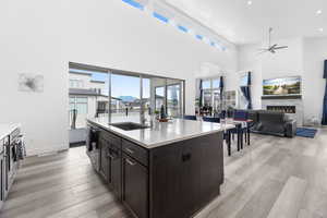 Kitchen with a warm lit fireplace, light countertops, light wood finished floors, and a sink