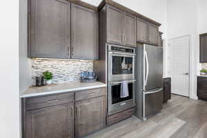 Kitchen featuring tasteful backsplash, light countertops, appliances with stainless steel finishes, light wood-style floors, and dark brown cabinets