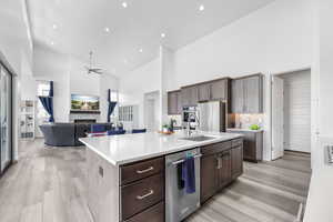 Kitchen with stainless steel appliances, light countertops, light wood-style floors, a stone fireplace, and high vaulted ceiling