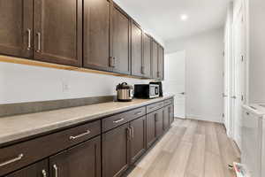 Kitchen featuring washer / clothes dryer, stainless steel microwave, light wood-style flooring, dark brown cabinetry, and baseboards
