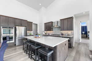 Kitchen with dark brown cabinetry, a breakfast bar area, appliances with stainless steel finishes, wall chimney range hood, and a sink