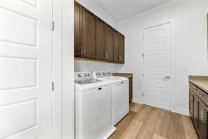 Laundry room featuring baseboards, light wood-style floors, cabinet space, and washer and dryer