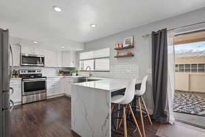 Beautifully remodeled kitchen featuring white quartz countertops, stainless steel electric appliances, white cabinetry, a peninsula, and a kitchen bar.