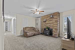 Carpeted living room featuring a textured ceiling, ceiling fan, a wood stove, and baseboards