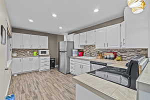 Kitchen featuring stainless steel appliances, a sink, light wood-style flooring, and white cabinets