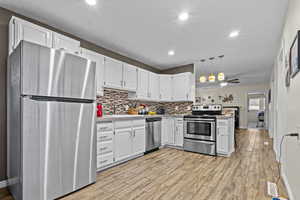 Kitchen featuring light wood-style floors, white cabinets, light countertops, appliances with stainless steel finishes, and tasteful backsplash