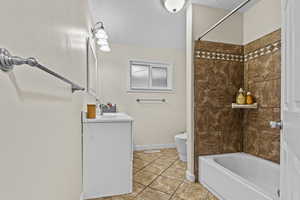 Bathroom with toilet, tub / shower combination, vanity, tile patterned flooring, and baseboards