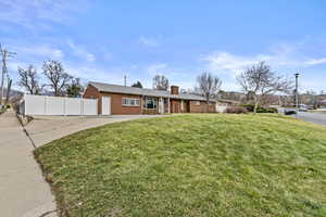 Ranch-style house featuring concrete driveway, a chimney, fence, a front lawn, and brick siding