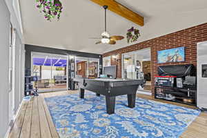 Game room with vaulted ceiling with beams, hardwood / wood-style flooring, brick wall, and ceiling fan