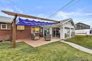 Rear view of property featuring fence, an outdoor hangout area, a lawn, and brick siding