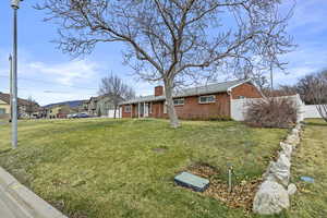 Ranch-style home with brick siding, a front lawn, a chimney, and fence