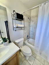 En-suite Full bathroom with shower / bath combination with curtain, toilet, vanity, a textured ceiling, and tile patterned flooring