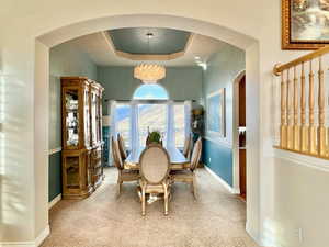 Formal Dining area with carpet floors, arched walkways, a raised ceiling, a chandelier, and baseboards