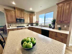 Kitchen with brown cabinetry, a sink, backsplash, and black appliances looking west to formal dining room