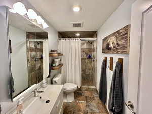 Comfortable bathroom featuring toilet, a shower stall, and stone tile floors