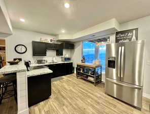 Kitchen featuring light wood finished floors, appliances with stainless steel finishes, a kitchen breakfast bar, a peninsula, and dark cabinetry